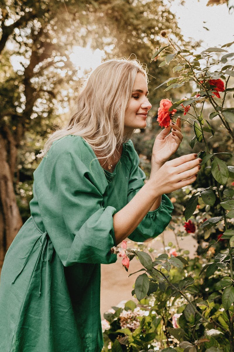 Woman Wearing a Green Long-sleeved Dress Smelling a Flower